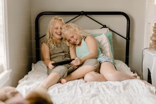 two young girls sitting on a bed with their arms around each other