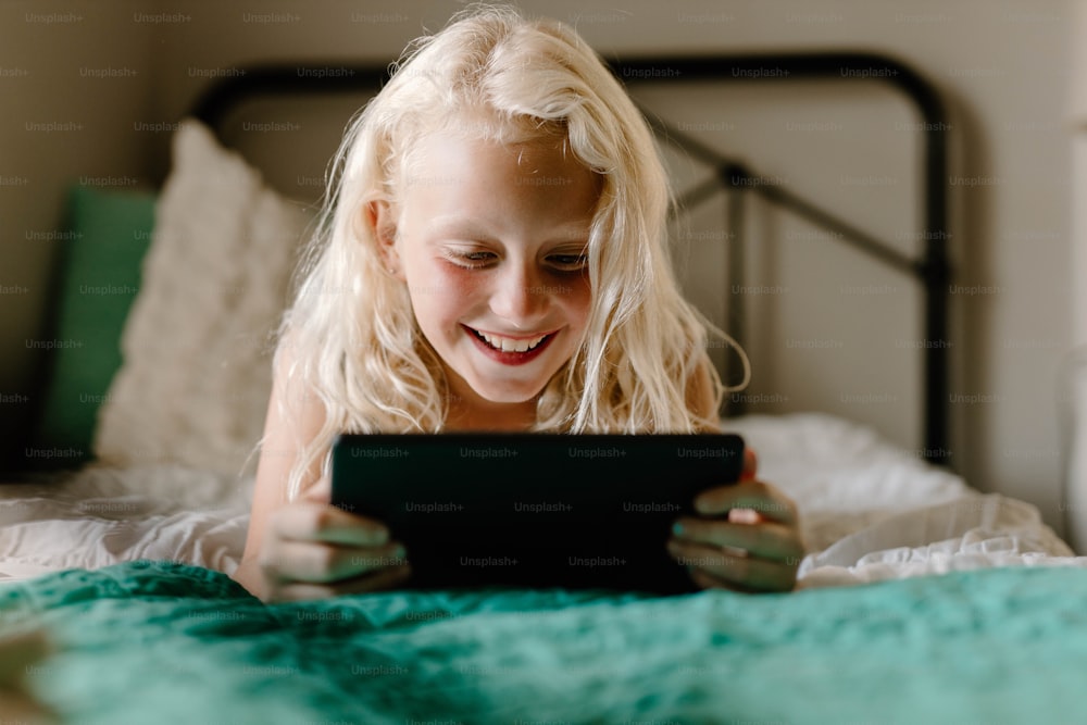 a little girl laying on a bed looking at a tablet