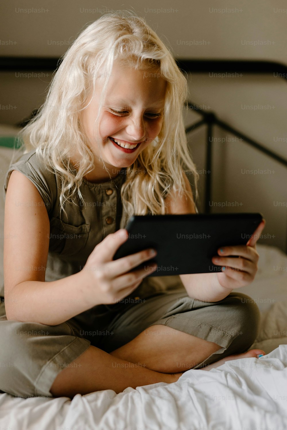 a little girl sitting on a bed looking at a tablet