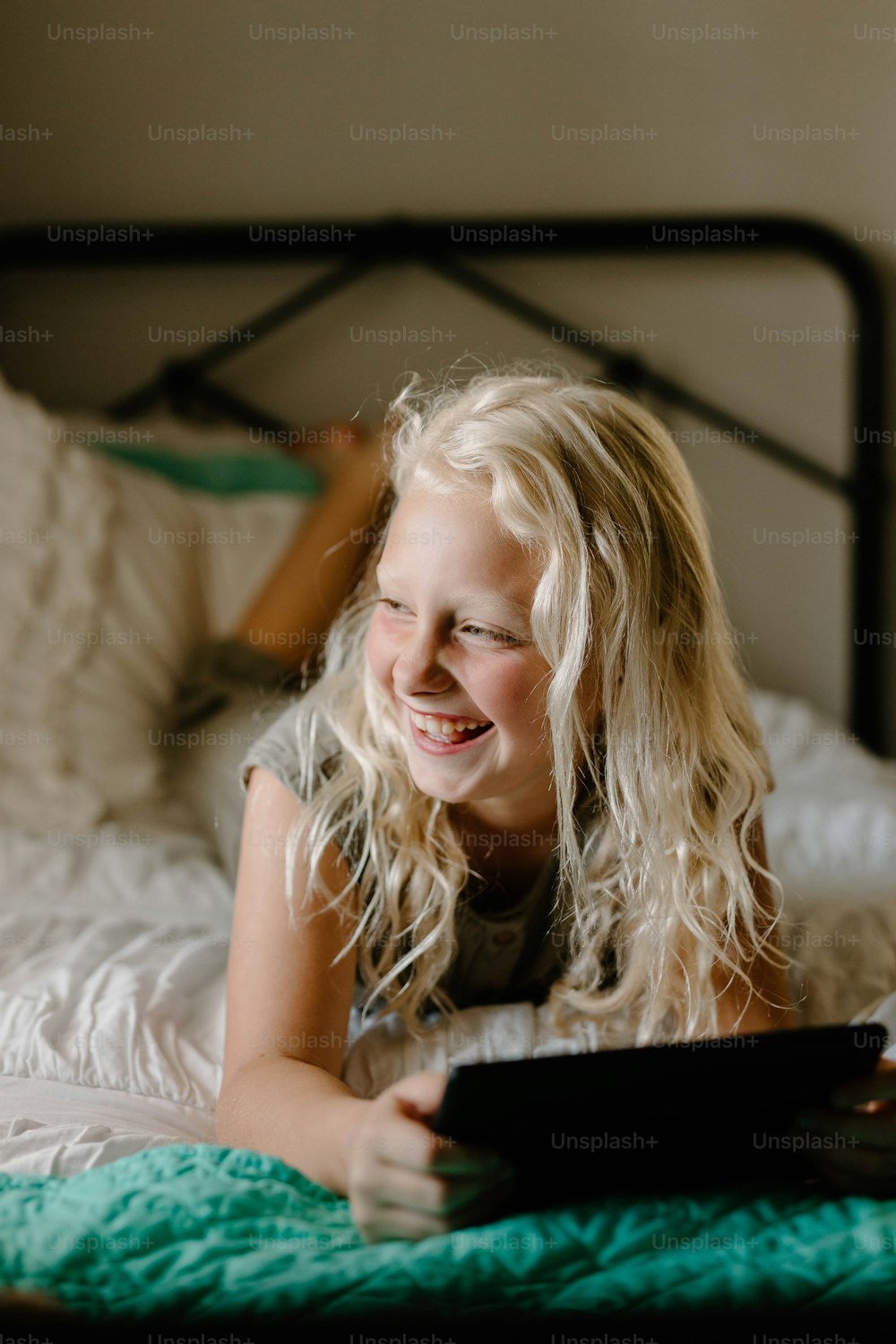 a little girl laying on a bed with a tablet