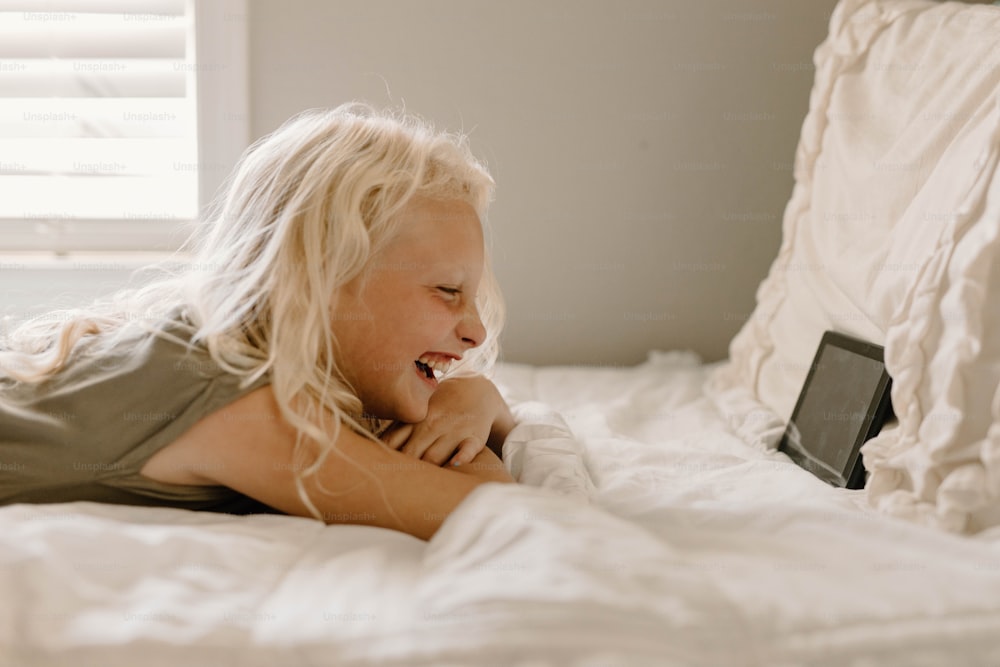 a little girl laying on a bed with a laptop
