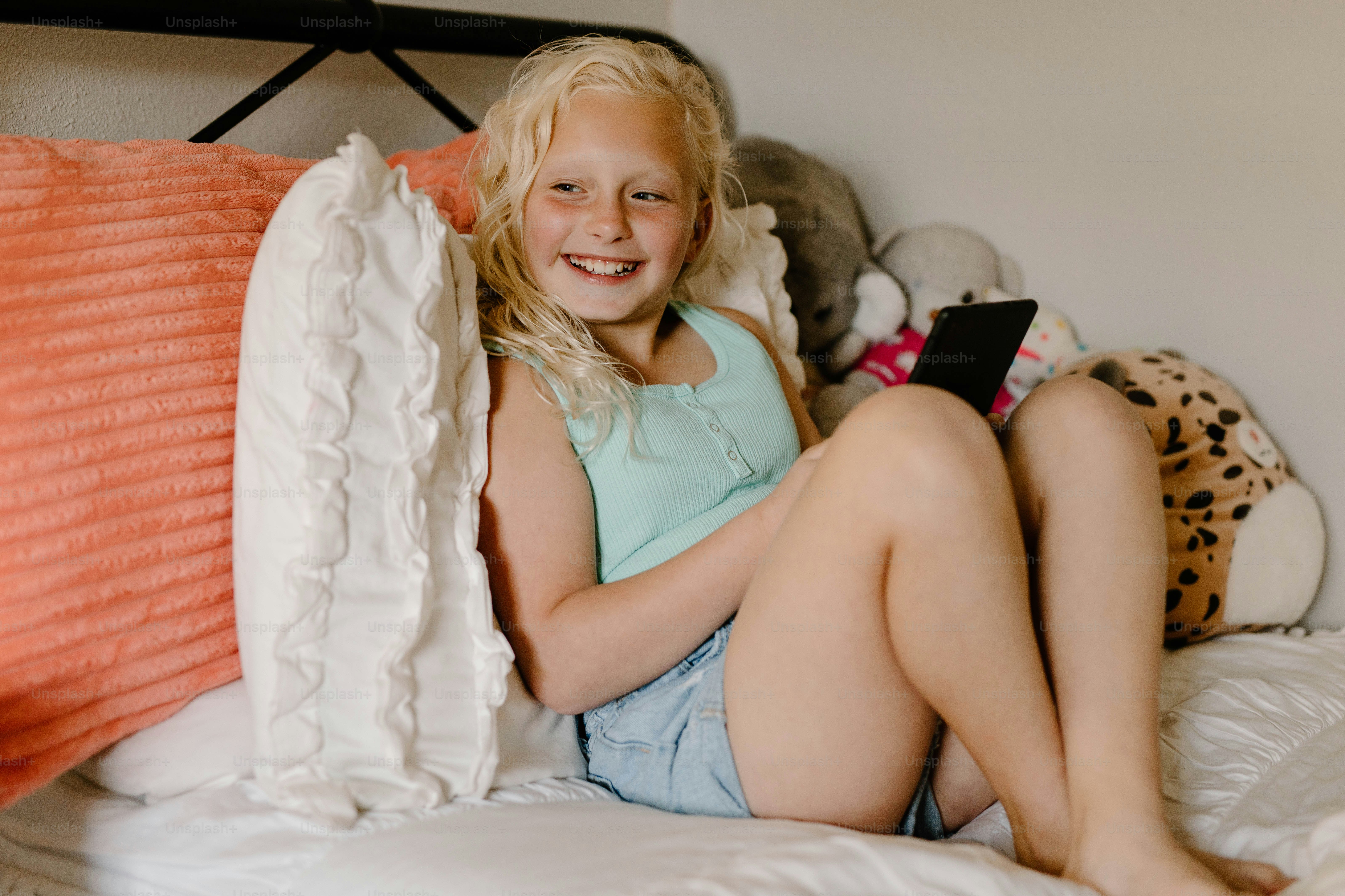 a young girl sitting on a bed holding a cell phone