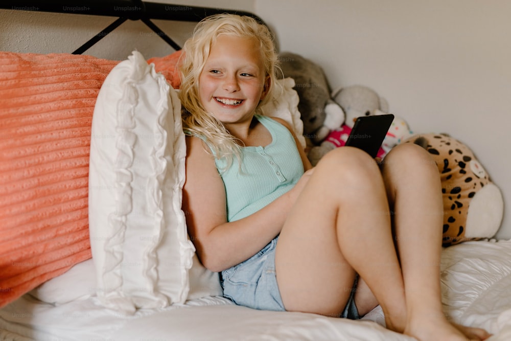 a young girl sitting on a bed holding a cell phone