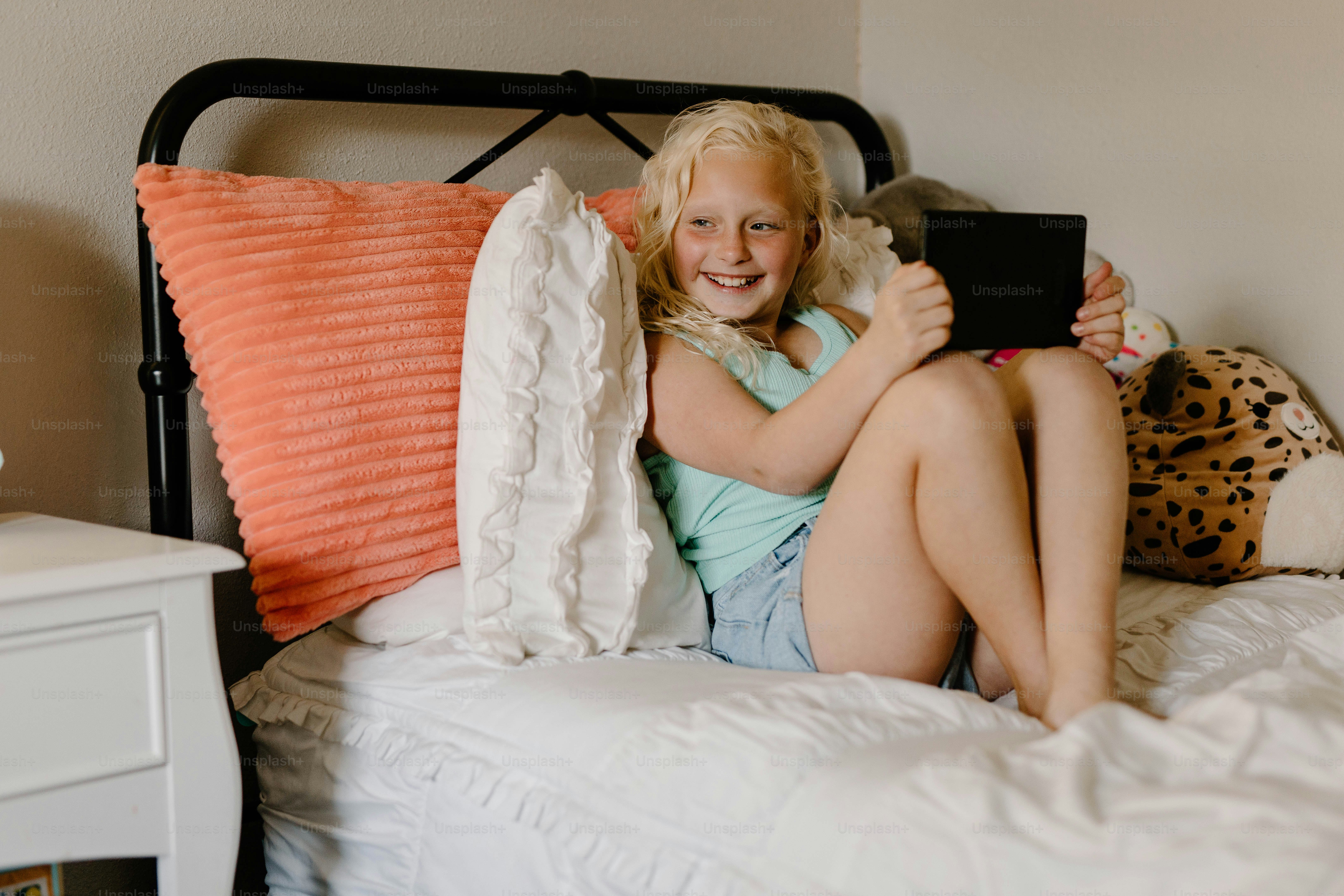 a little girl sitting on a bed holding a tablet