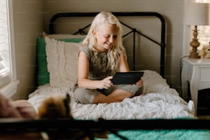 a little girl sitting on a bed playing with a tablet