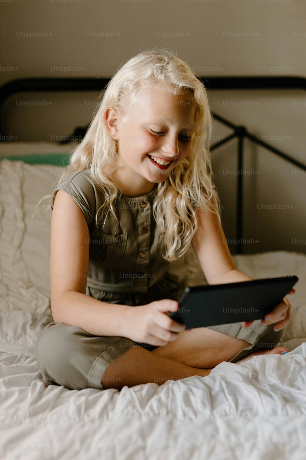 a little girl sitting on a bed playing with a tablet
