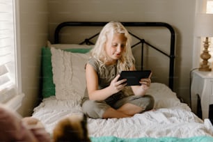 a little girl sitting on a bed looking at a tablet