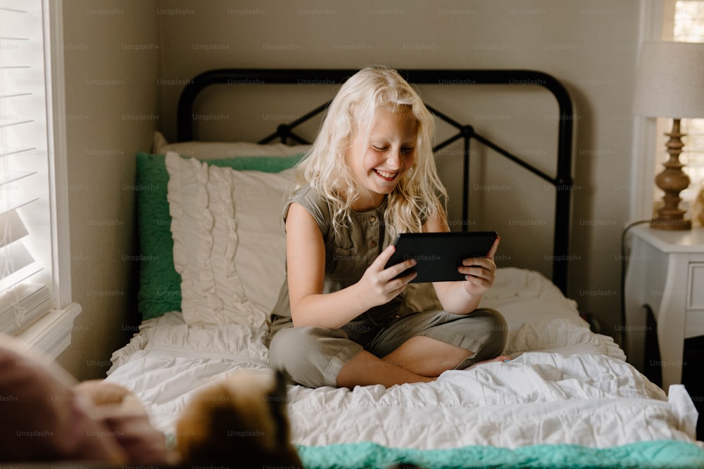 a little girl sitting on a bed playing with a tablet