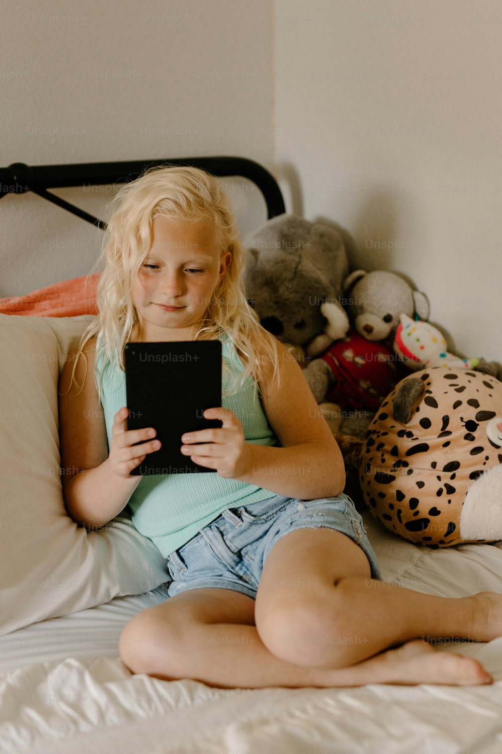 a little girl sitting on a bed holding a tablet