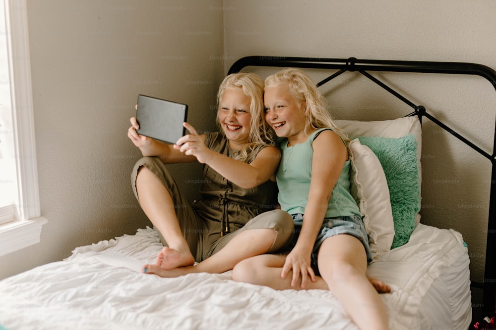 two young girls sitting on a bed looking at a tablet
