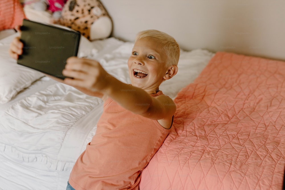 a young boy laying on a bed holding a tablet