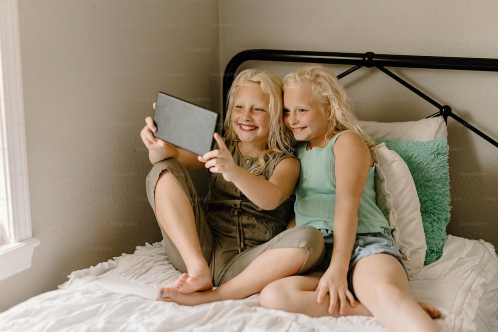 two little girls sitting on a bed with a tablet