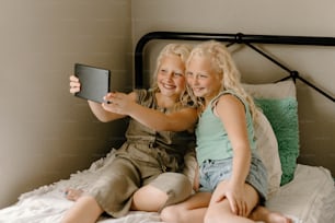 Zwei kleine Mädchen, die auf einem Bett sitzen und ein Foto machen