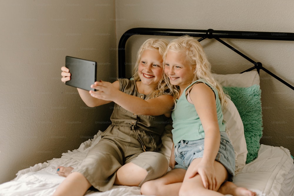 two little girls sitting on a bed taking a picture