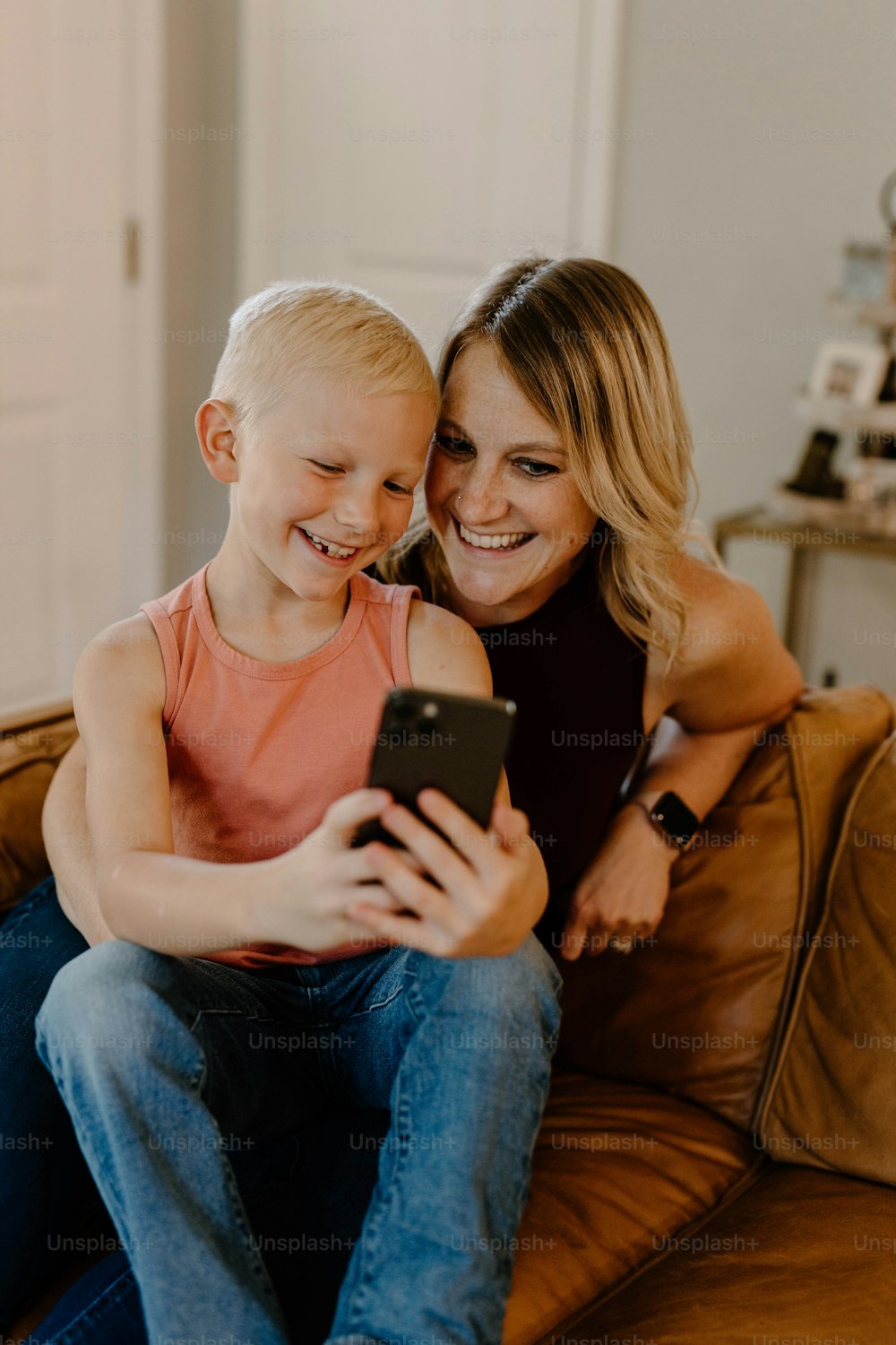 a woman and a child sitting on a couch looking at a cell phone