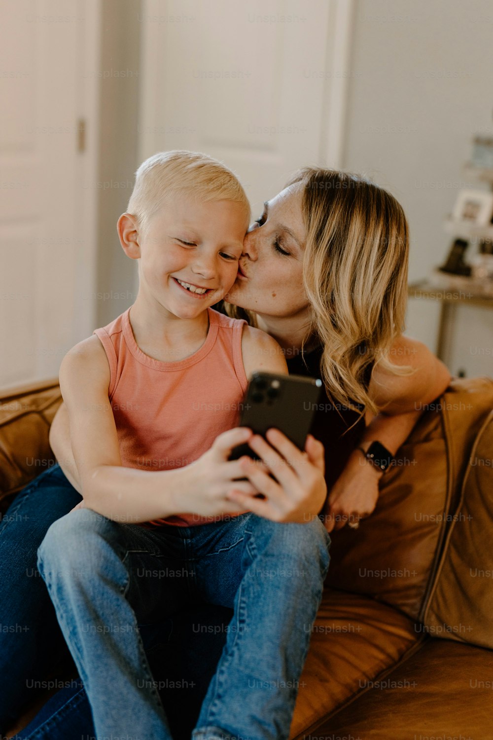 a woman sitting on a couch kissing a little boy