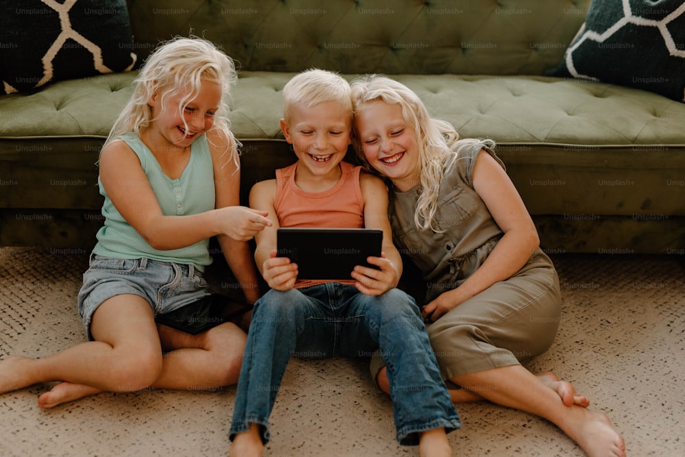 three young girls sitting on the floor looking at a tablet
