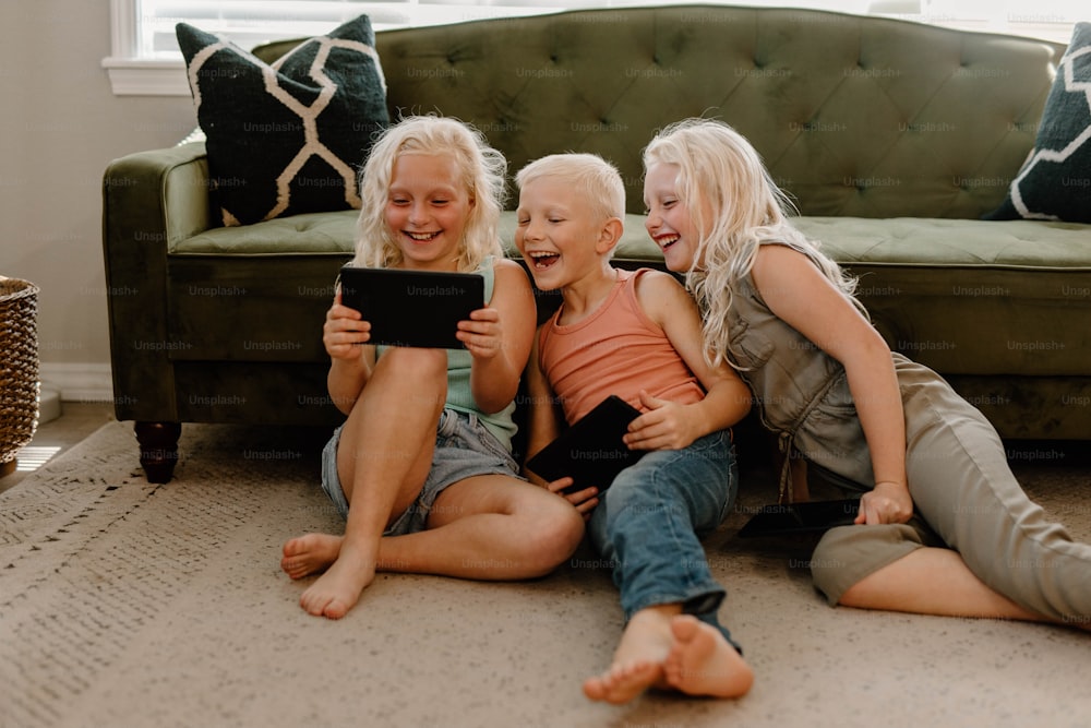 three girls and a boy sitting on the floor looking at a tablet