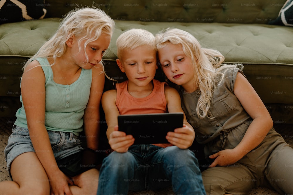 três crianças sentadas no chão olhando para um tablet
