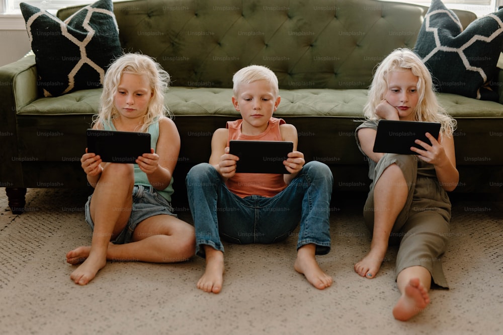 Drei kleine Mädchen, die mit ihren iPads auf dem Boden sitzen