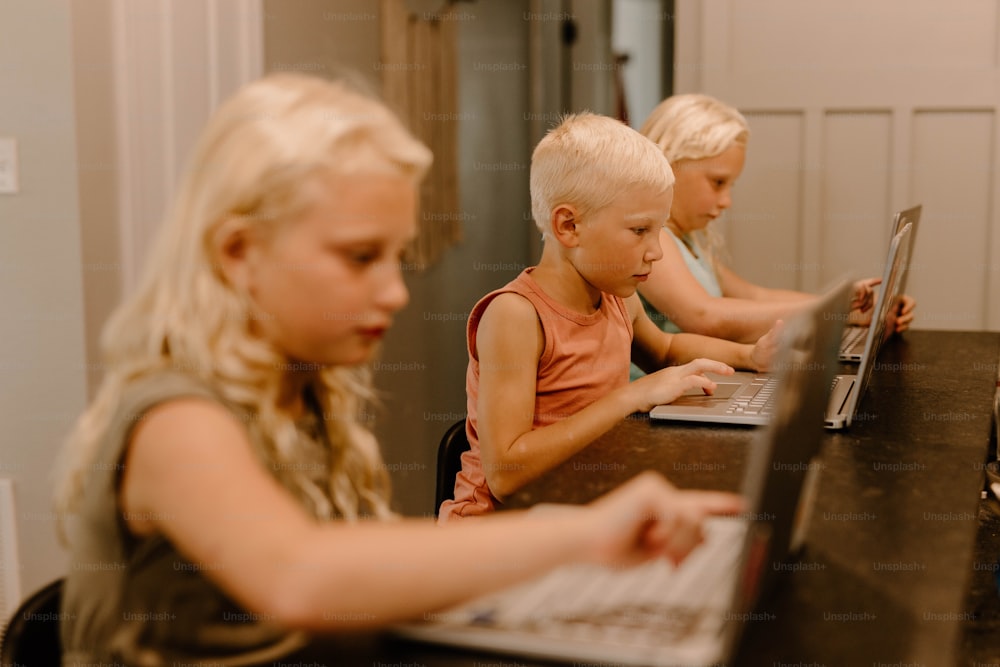 한 무리의 어린이들이 탁자에 앉아 노트북 컴퓨터를 사용하고 있다