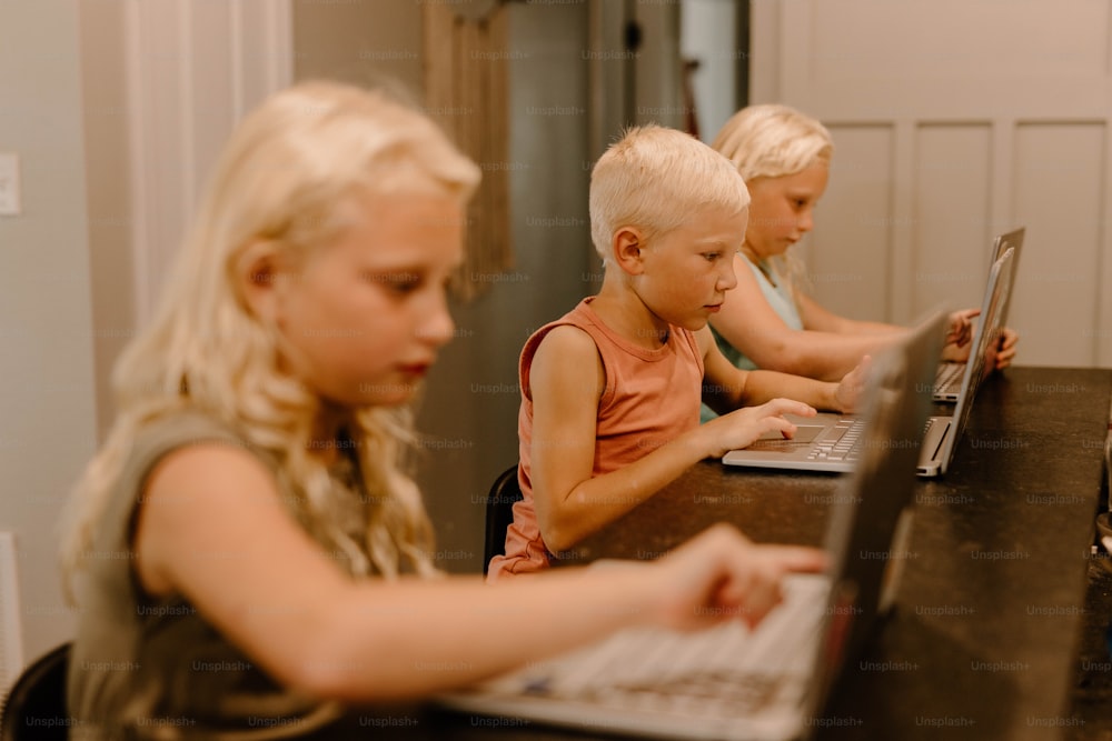 a group of children sitting at a table using laptop computers