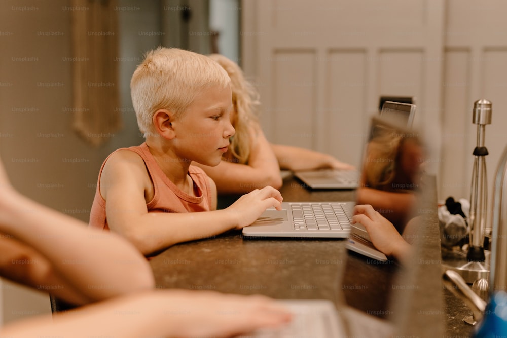 a young boy sitting at a table using a laptop computer