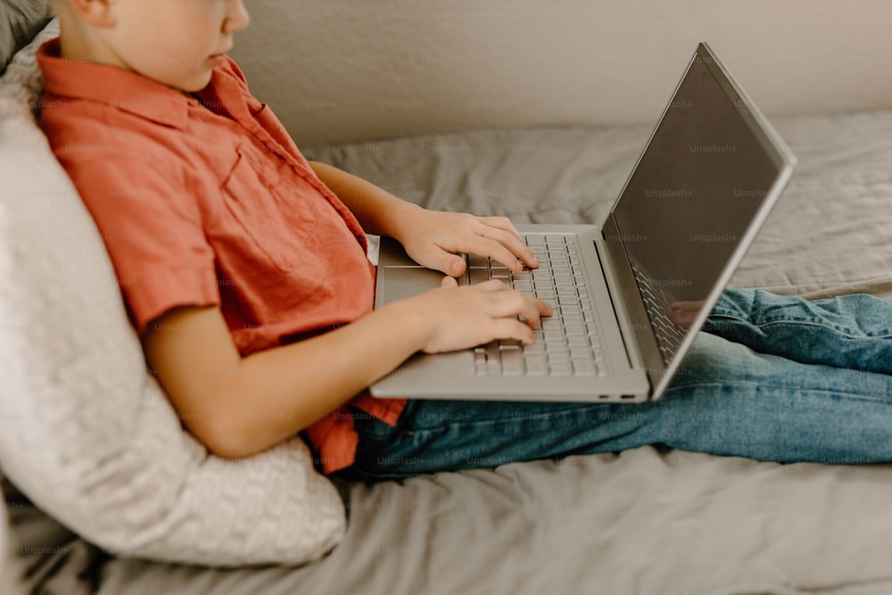 um menino sentado em uma cama usando um computador portátil