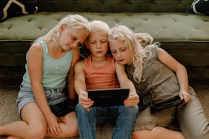 Drei kleine Mädchen, die auf dem Boden sitzen und auf ein Tablet schauen