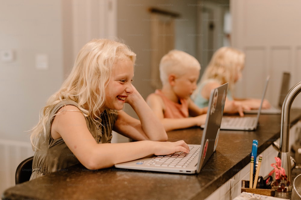 부엌 카운터에 앉아 노트북 컴퓨터를 사용하는 어린 소녀