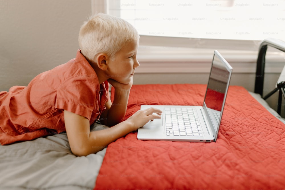 a young boy laying on a bed using a laptop computer