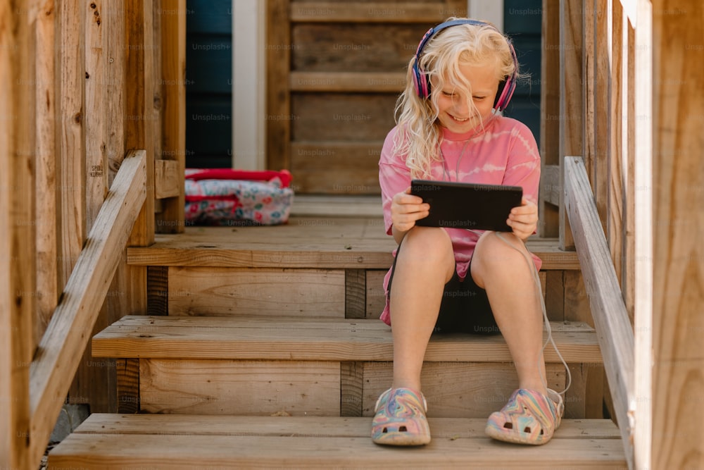 a little girl sitting on a set of steps using a tablet