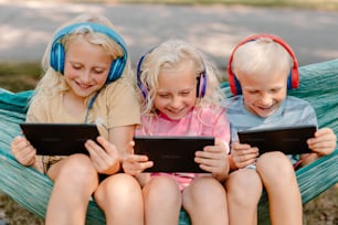Drei Kinder sitzen in einer Hängematte mit Kopfhörern