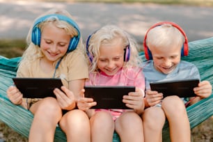 three children sitting in a hammock with headphones on