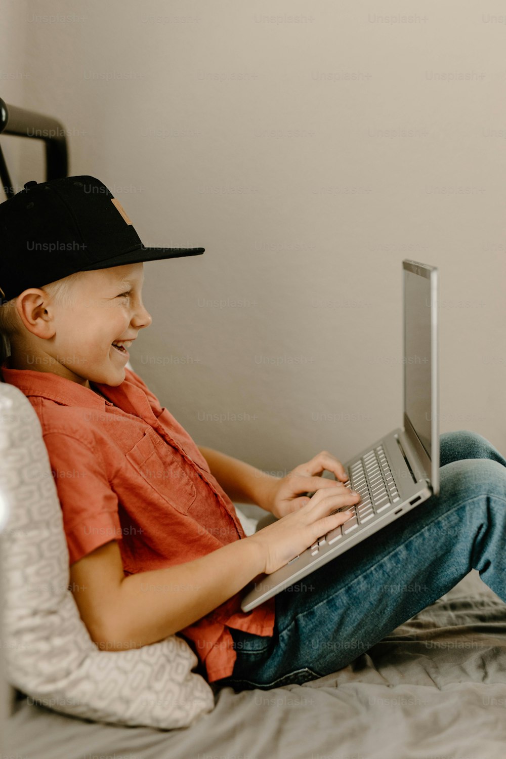 a young boy sitting on a bed using a laptop computer