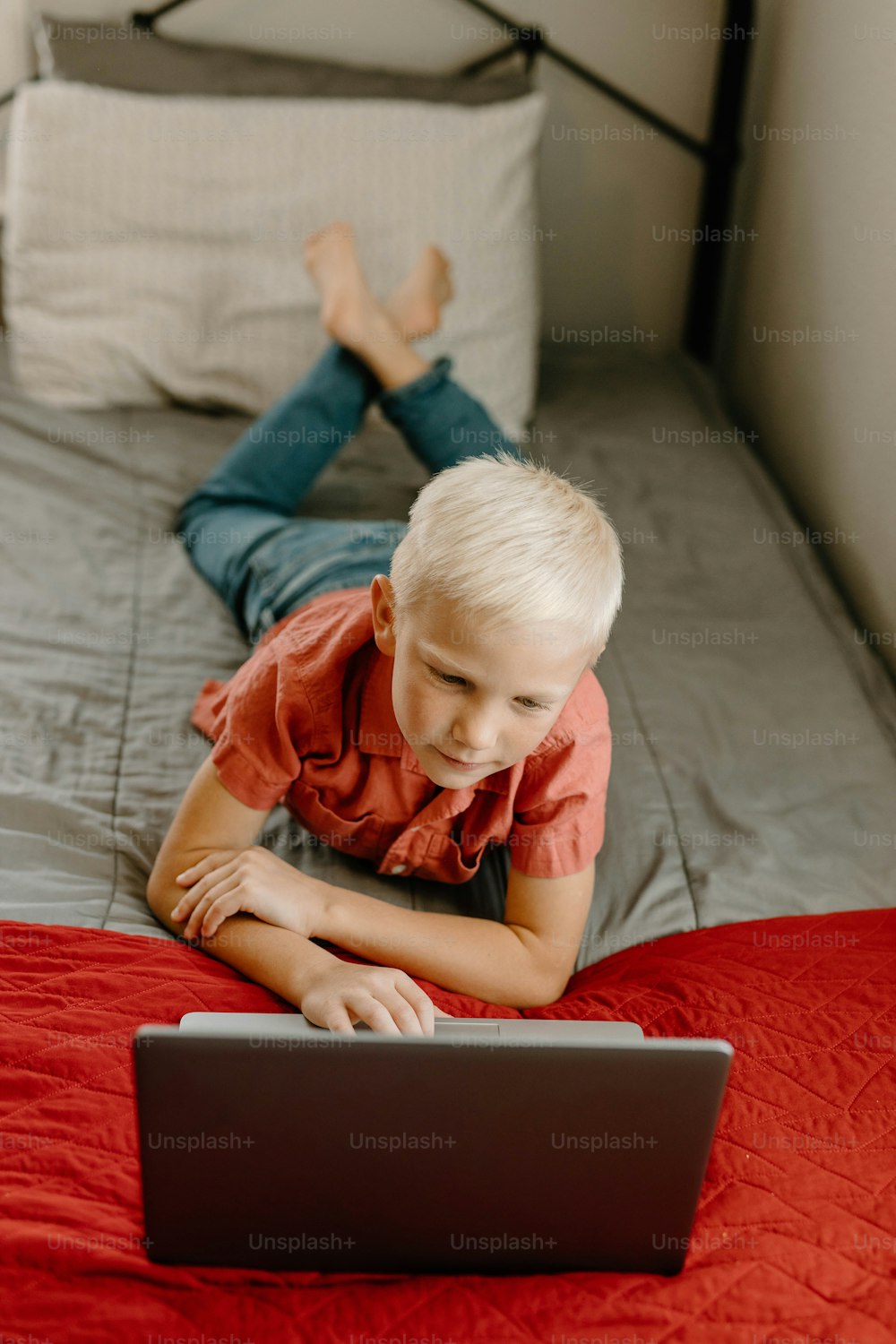 Ein kleiner Junge, der mit einem Laptop auf einem Bett liegt