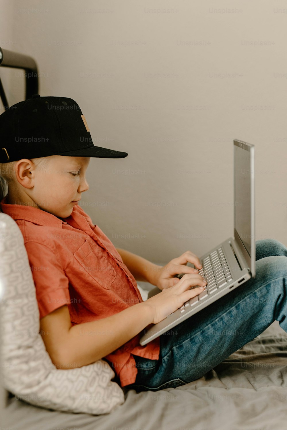 노트북 컴퓨터를 사용하여 침대에 앉아 있는 어린 소년