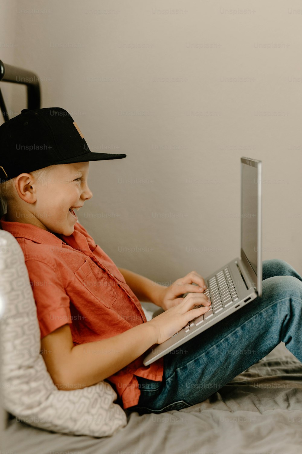 Ein kleiner Junge, der mit einem Laptop auf einem Bett sitzt