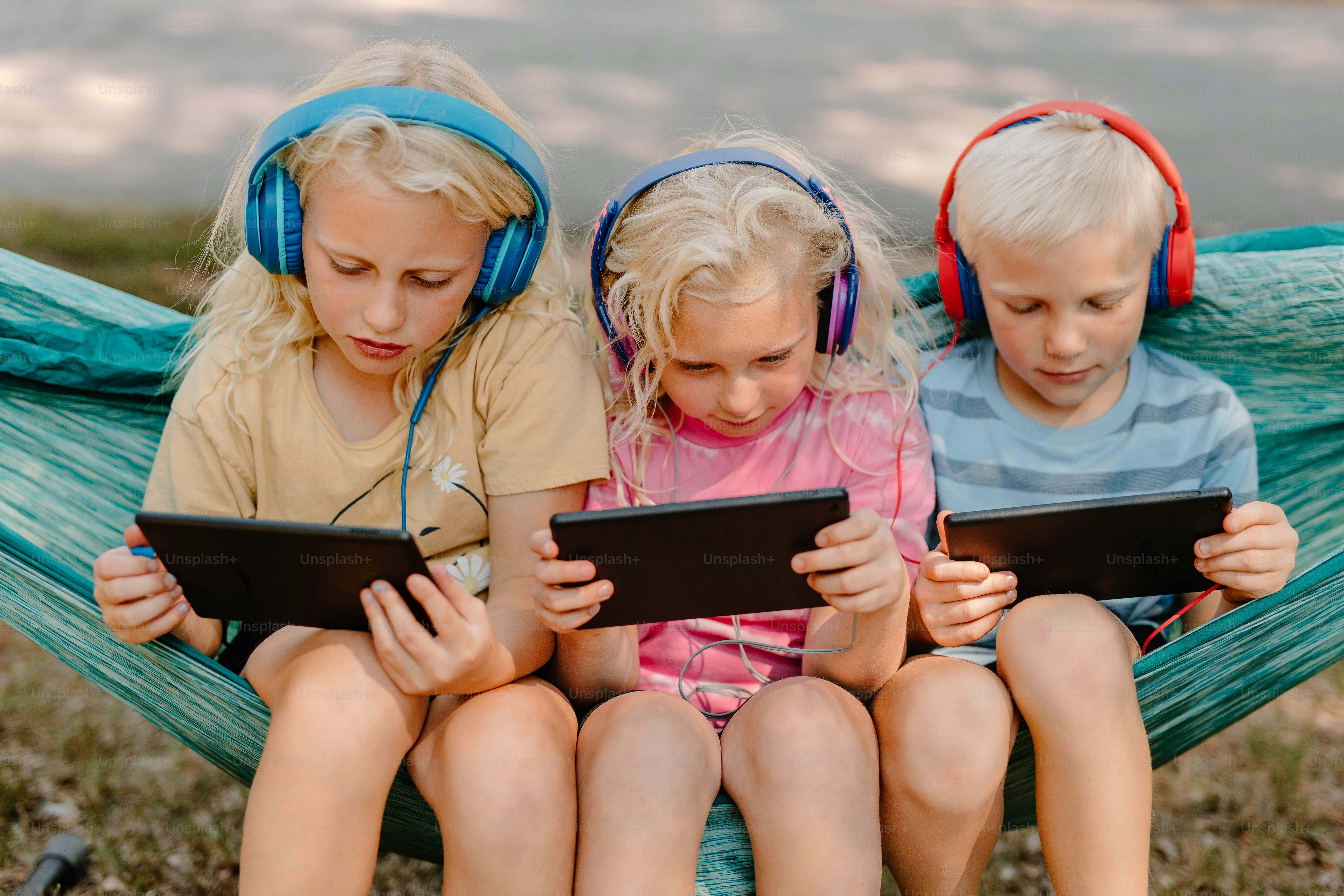 three children sitting in a hammock with headphones on