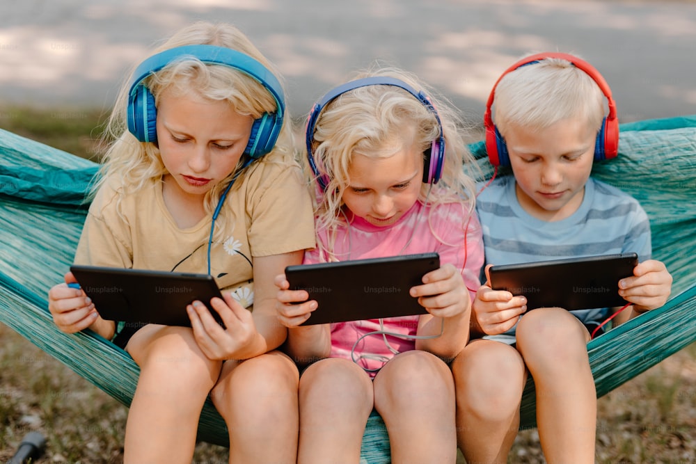 Tres niños sentados en una hamaca con auriculares puestos