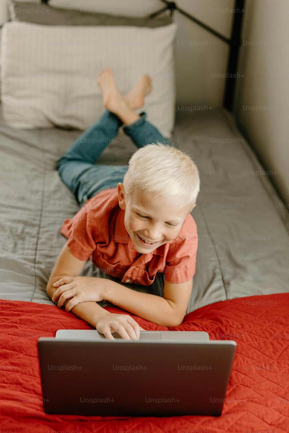a young boy laying on a bed using a laptop