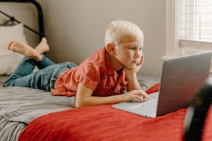 a little boy laying on a bed with a laptop