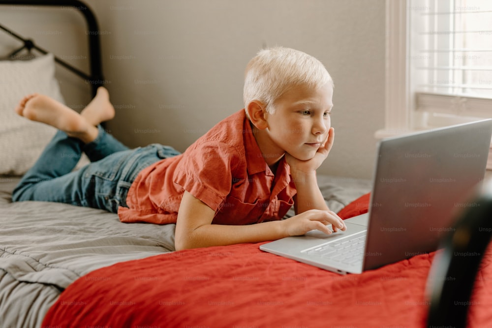 a little boy laying on a bed with a laptop