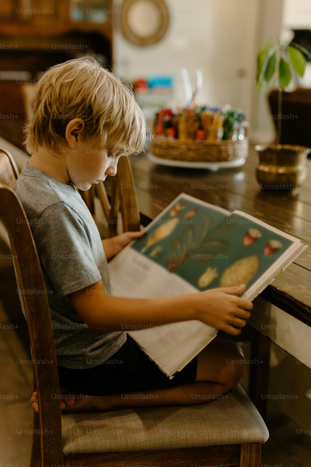 a young boy sitting at a table reading a book