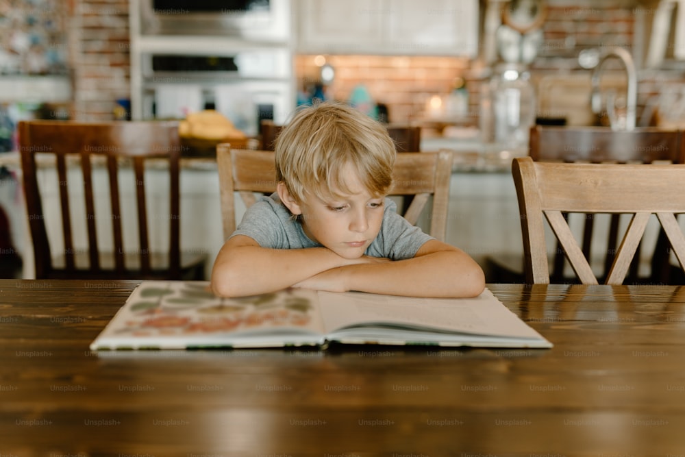 a young boy sitting at a table reading a book