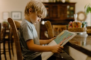 a young boy sitting at a table reading a book