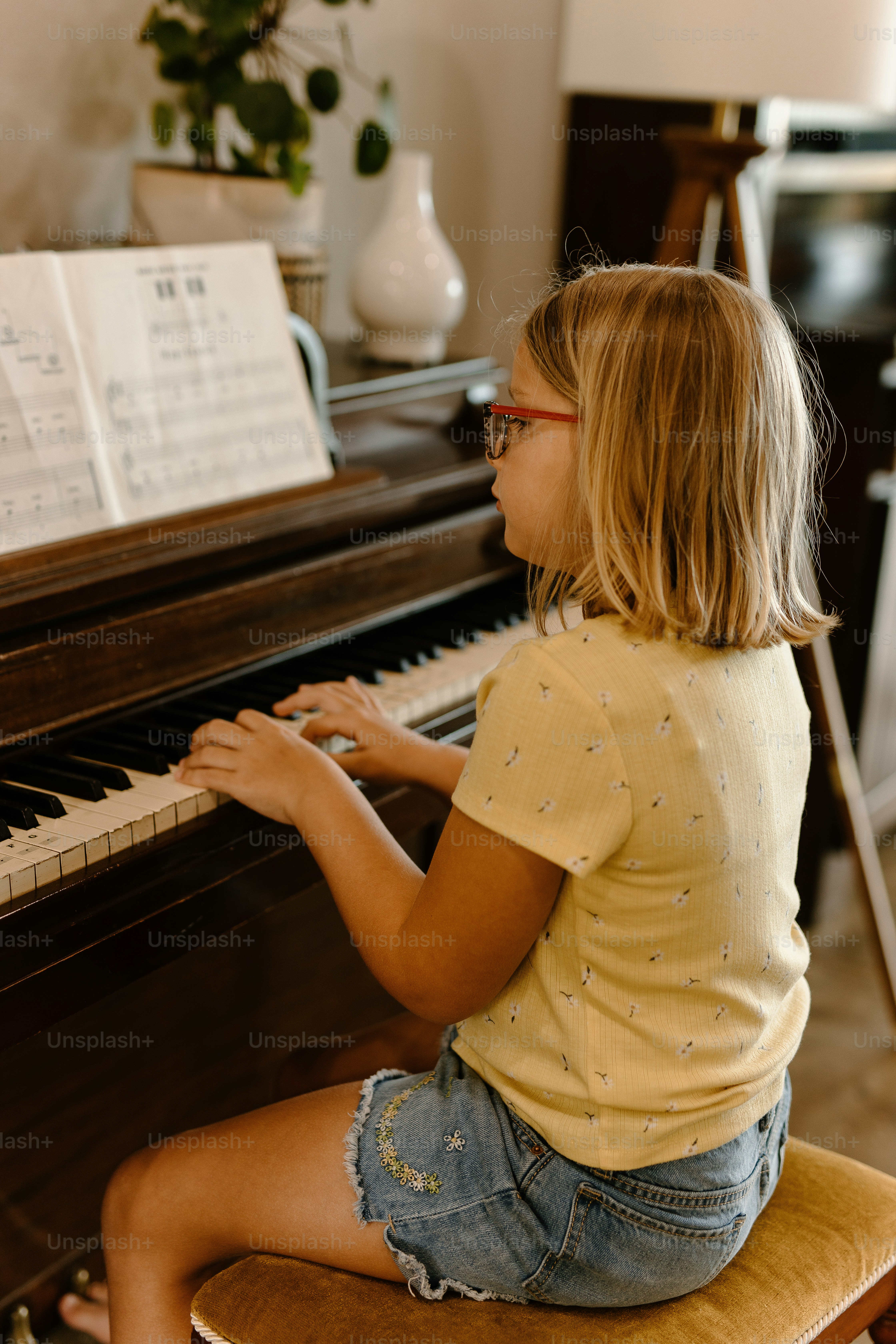 a little girl sitting on a stool playing a piano