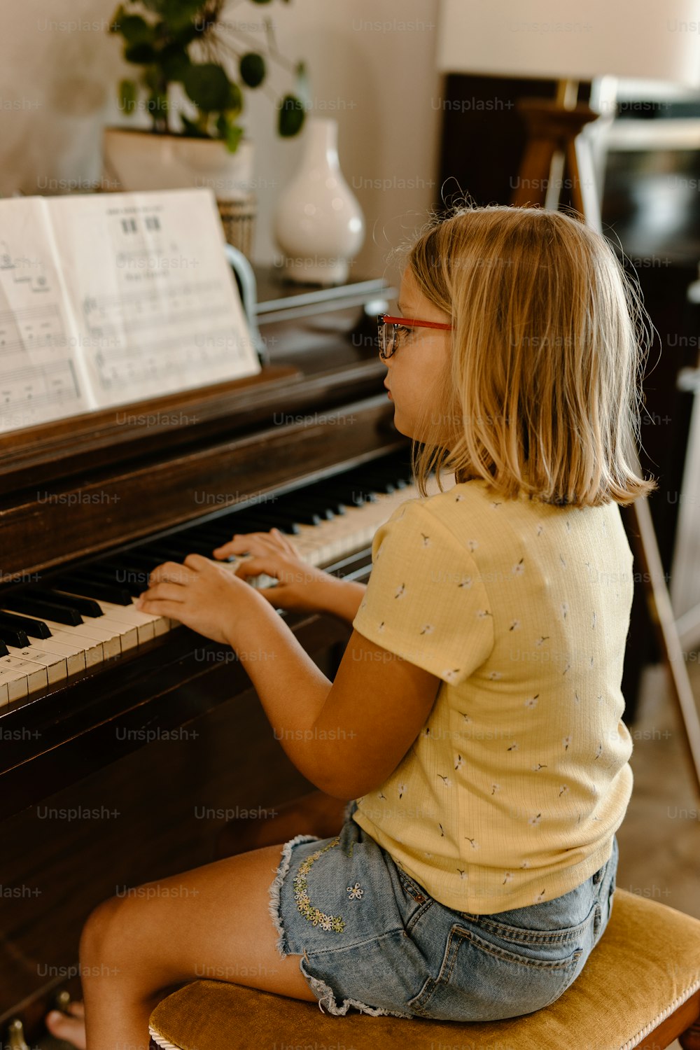a little girl sitting on a stool playing a piano