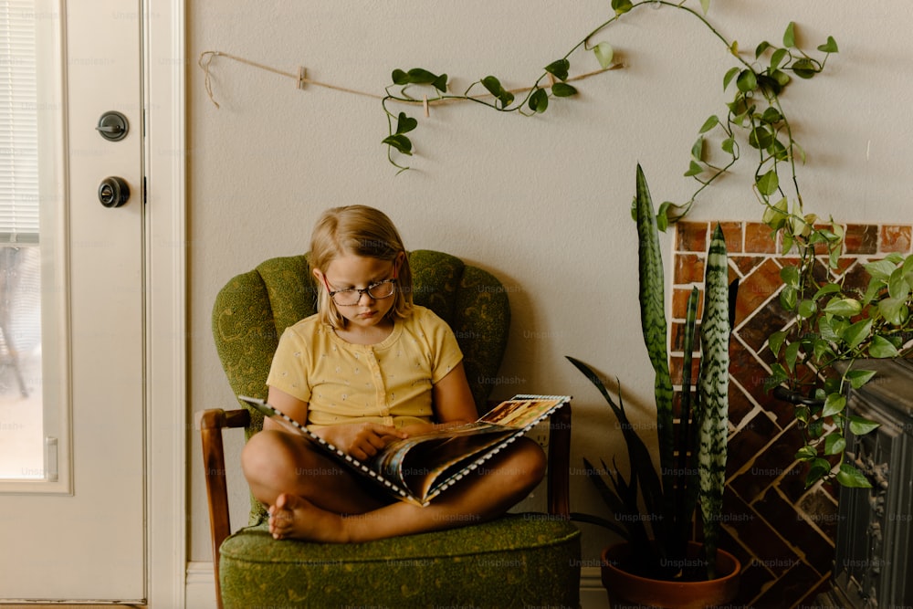 a little girl sitting in a chair reading a book