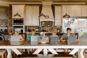 a group of kids sitting at a table with laptops